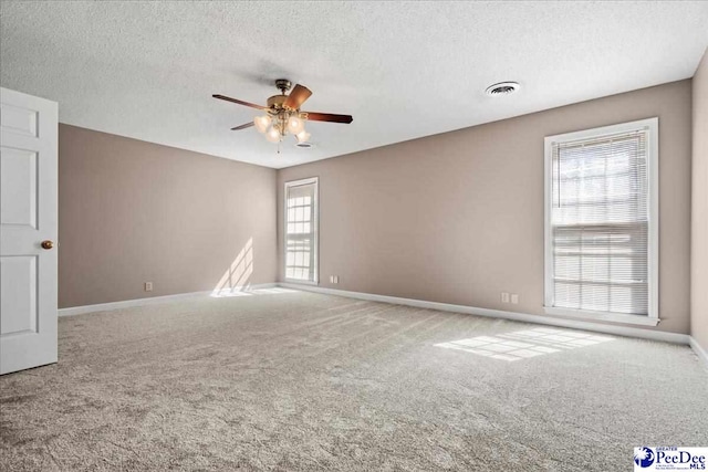 carpeted spare room featuring ceiling fan, visible vents, baseboards, and a textured ceiling