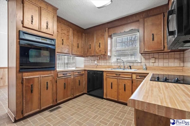 kitchen with a sink, brick patterned floor, black appliances, tasteful backsplash, and brown cabinetry