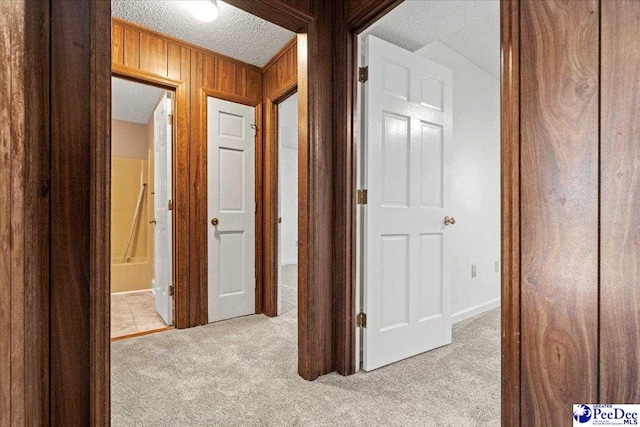 hallway featuring wood walls, a textured ceiling, and light colored carpet