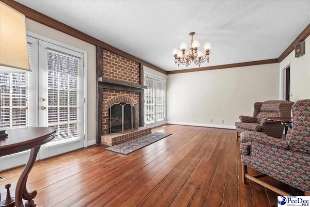 living room featuring baseboards, hardwood / wood-style floors, crown molding, a textured ceiling, and a brick fireplace