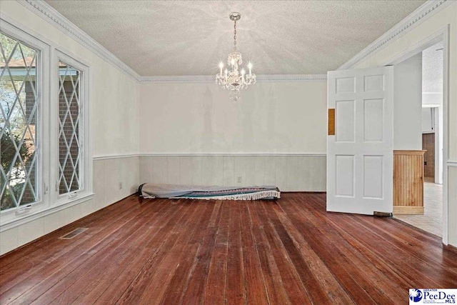 unfurnished room with plenty of natural light, wainscoting, hardwood / wood-style flooring, crown molding, and a notable chandelier