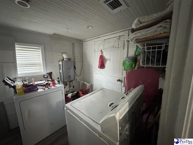washroom featuring water heater, laundry area, wood walls, visible vents, and washer and clothes dryer