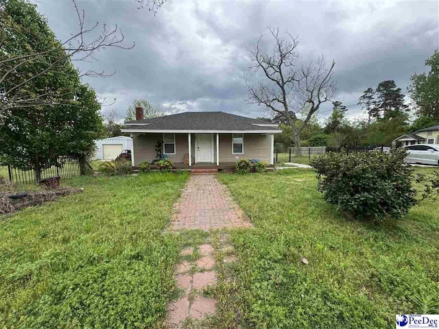 bungalow with fence, a chimney, covered porch, and a front lawn