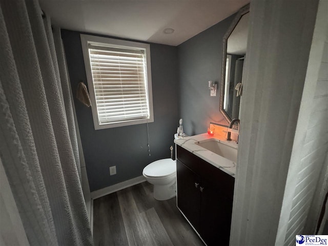 bathroom with toilet, vanity, wood finished floors, and baseboards