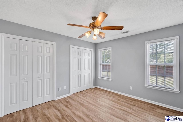 unfurnished bedroom with ceiling fan, a textured ceiling, light hardwood / wood-style floors, and multiple closets