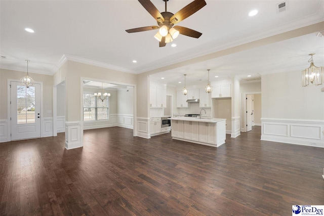 unfurnished living room with sink, ornamental molding, dark hardwood / wood-style flooring, and ceiling fan with notable chandelier