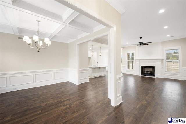 unfurnished living room featuring dark wood-type flooring, a healthy amount of sunlight, coffered ceiling, and ceiling fan with notable chandelier