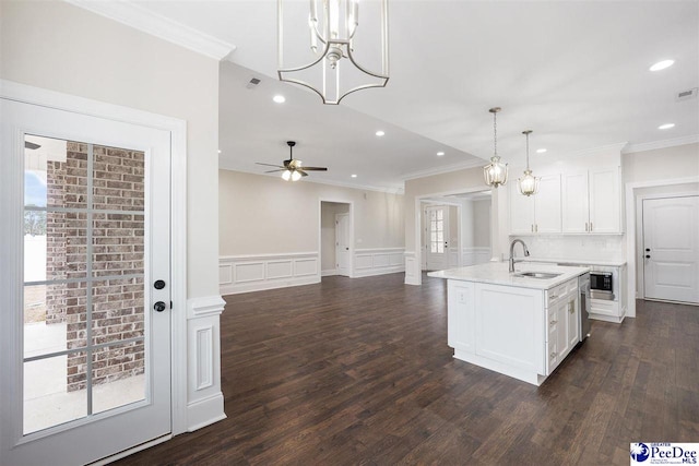 kitchen with sink, white cabinets, hanging light fixtures, dark wood-type flooring, and a center island with sink