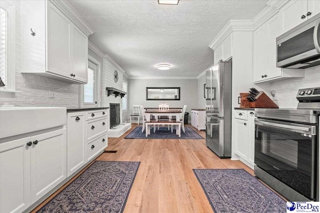 3900 Claussen Rd, Florence, SC 29505 - kitchen featuring appliances with stainless steel finishes, light wood finished floors, white cabinetry, a textured ceiling, and decorative backsplash