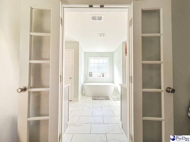 full bath with marble finish floors, a freestanding bath, and baseboards