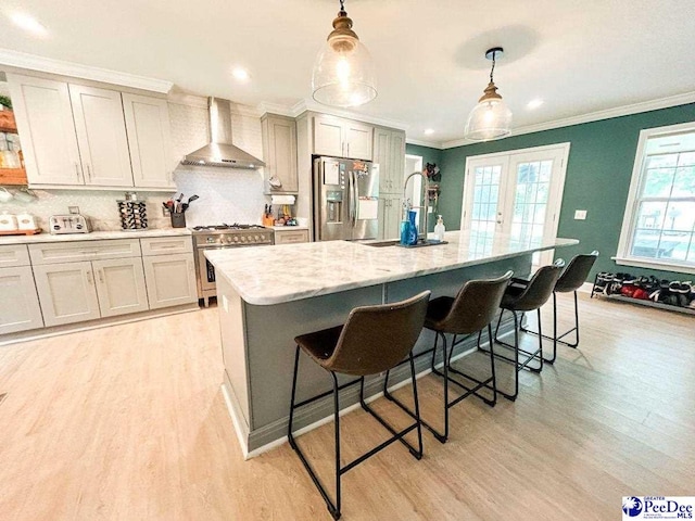 kitchen featuring appliances with stainless steel finishes, wall chimney exhaust hood, ornamental molding, light wood-style floors, and a breakfast bar