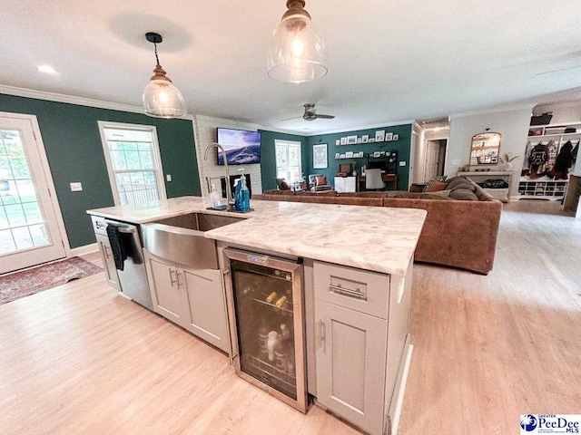 kitchen with wine cooler, light wood-style floors, a sink, crown molding, and hanging light fixtures