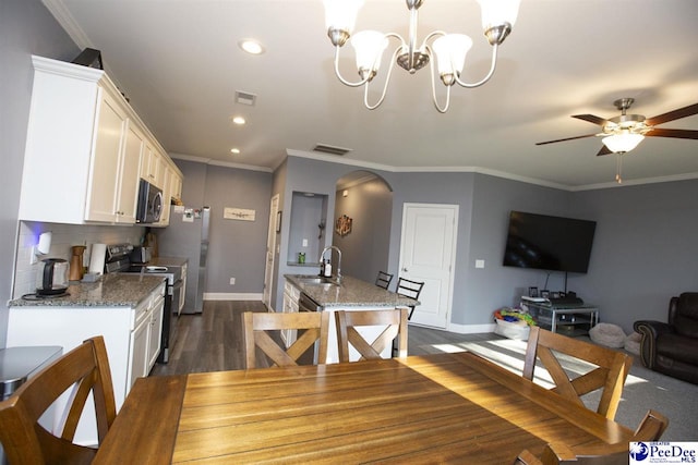 dining area with dark wood-type flooring, ornamental molding, ceiling fan with notable chandelier, and sink