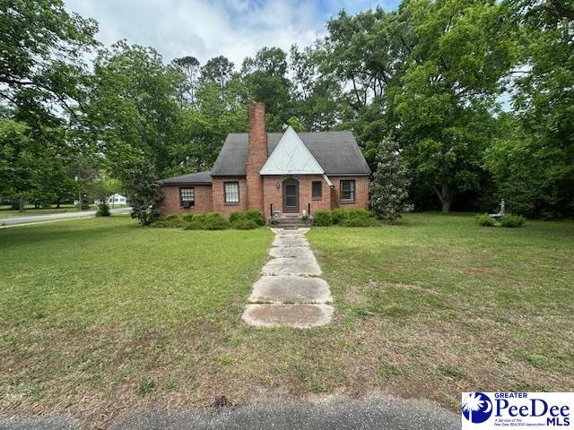 tudor home featuring a front lawn, brick siding, a chimney, and view of scattered trees