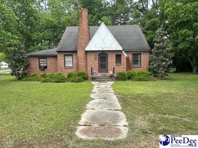 english style home with a front lawn, a chimney, and brick siding