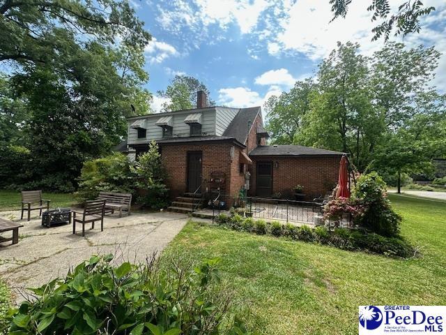 back of property featuring an outdoor fire pit, brick siding, a yard, a chimney, and a patio
