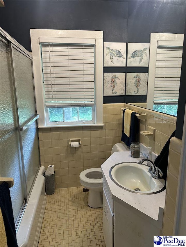 full bathroom featuring toilet, tile walls, vanity, shower / bath combination with glass door, and a wainscoted wall