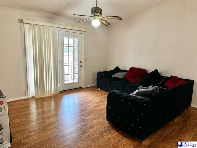 living room featuring a ceiling fan, a textured ceiling, baseboards, and wood finished floors