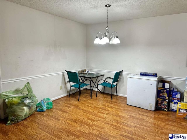 dining space featuring baseboards, a textured ceiling, wood finished floors, and an inviting chandelier