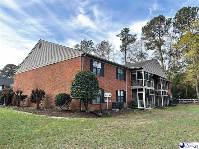 view of home's exterior with a sunroom, brick siding, and a yard
