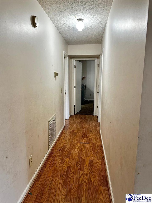 hallway featuring baseboards, visible vents, wood finished floors, and a textured ceiling