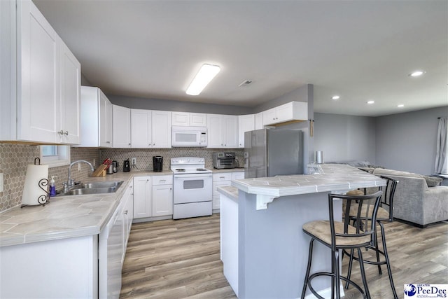 kitchen with open floor plan, tile countertops, a breakfast bar, white appliances, and a sink