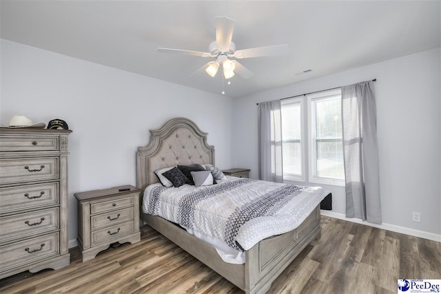 bedroom featuring ceiling fan, visible vents, baseboards, and wood finished floors