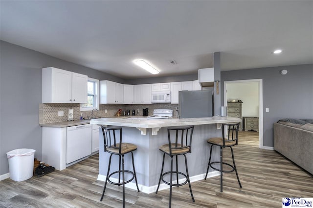 kitchen with white appliances, decorative backsplash, light countertops, white cabinets, and a kitchen bar