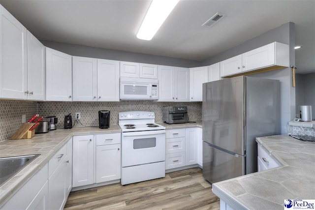 kitchen featuring light wood-type flooring, visible vents, white appliances, white cabinets, and tile counters