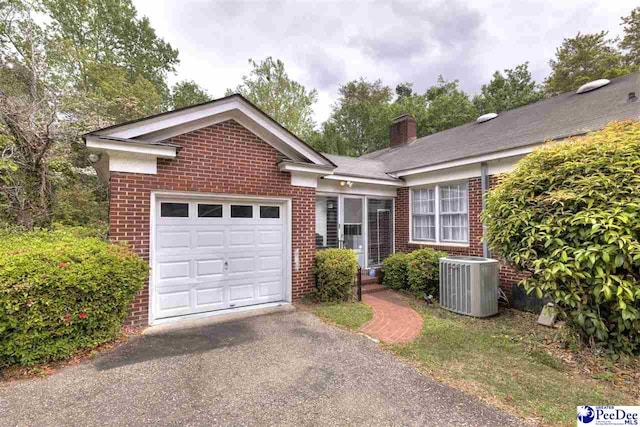 ranch-style house with a chimney, aphalt driveway, brick siding, central AC, and a garage