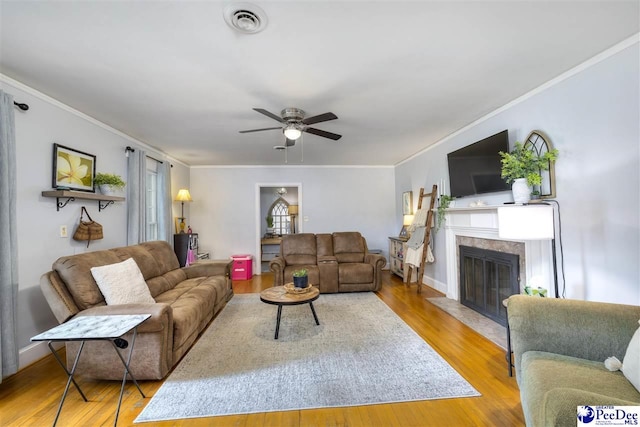 living room featuring ceiling fan, a fireplace with flush hearth, ornamental molding, visible vents, and wood finished floors
