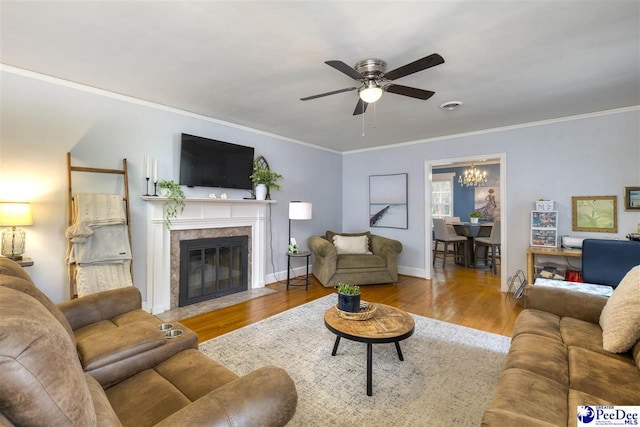 living room featuring baseboards, a fireplace, crown molding, wood finished floors, and ceiling fan with notable chandelier