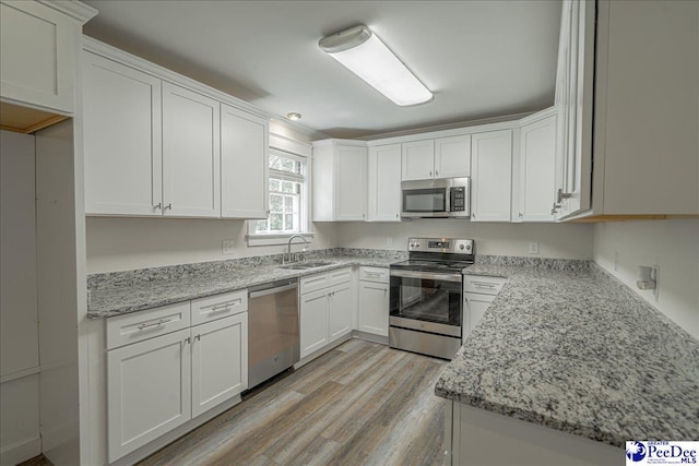 904 Madison Ave, Florence, SC 29501 - kitchen with appliances with stainless steel finishes, a sink, light wood-type flooring, white cabinetry, and light stone countertops