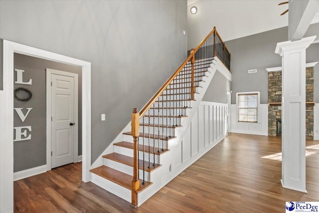 stairway with ornate columns, wood-type flooring, a fireplace, and a towering ceiling