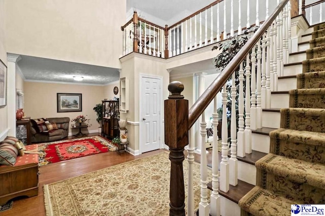 entrance foyer featuring a towering ceiling, wood-type flooring, and ornamental molding