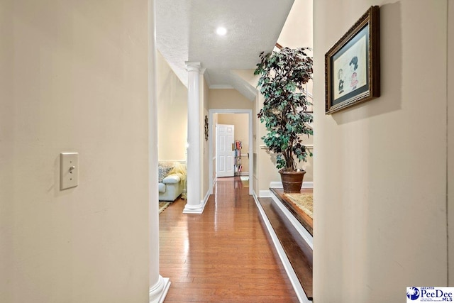 corridor with wood-type flooring, decorative columns, and a textured ceiling