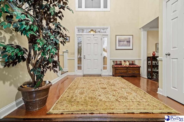 foyer entrance featuring wood-type flooring, decorative columns, and a high ceiling