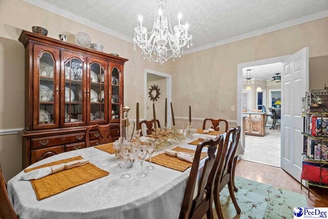 dining area with an inviting chandelier, ornamental molding, light hardwood / wood-style floors, and a textured ceiling