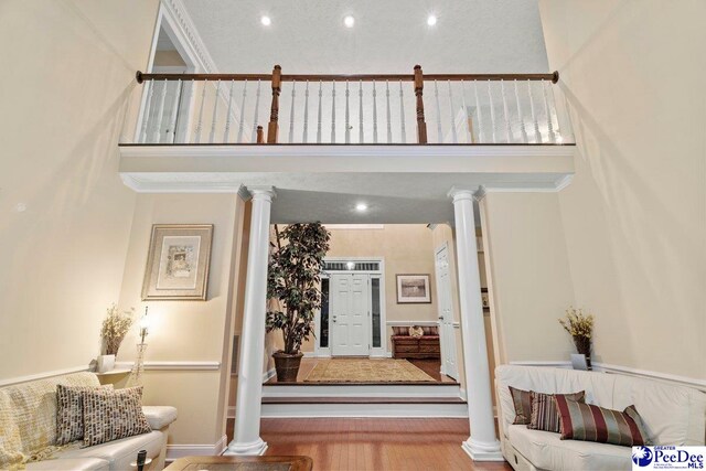 living room featuring hardwood / wood-style flooring, a towering ceiling, ornamental molding, and decorative columns