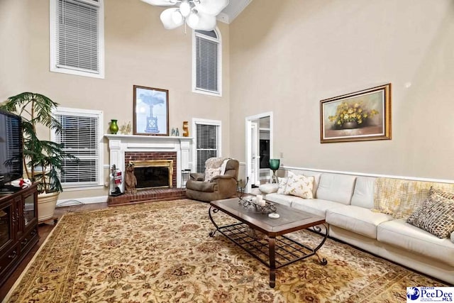 living room with a brick fireplace, a towering ceiling, hardwood / wood-style floors, and ceiling fan