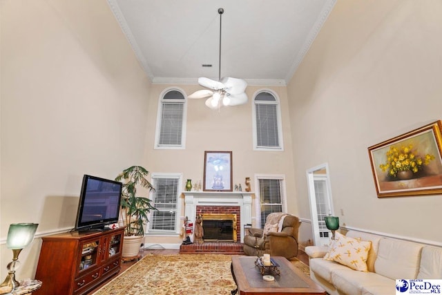 living room with a high ceiling, ornamental molding, ceiling fan, and a fireplace