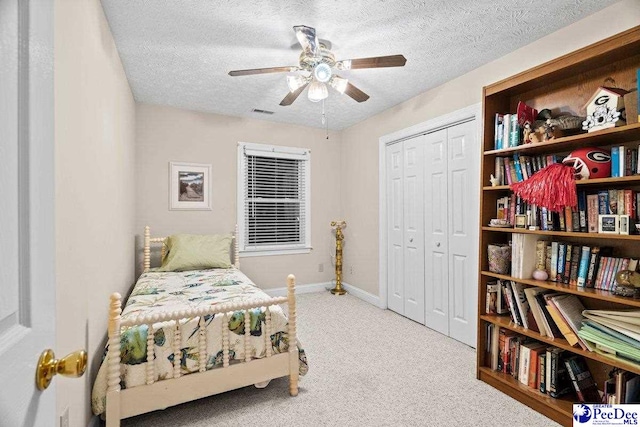 carpeted bedroom featuring ceiling fan, a closet, and a textured ceiling