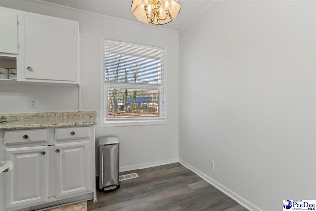 unfurnished dining area with baseboards, visible vents, dark wood finished floors, ornamental molding, and a chandelier