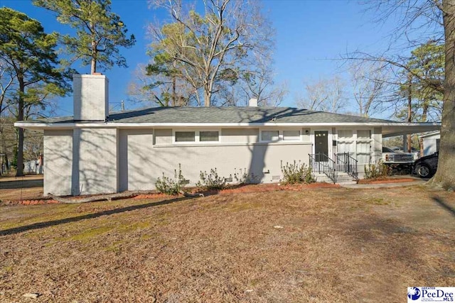 rear view of house featuring a lawn, an attached carport, a chimney, and brick siding