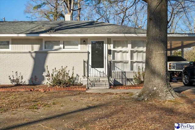 doorway to property featuring roof with shingles, a chimney, an attached carport, and brick siding