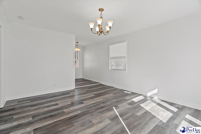 empty room with a chandelier, wood finished floors, and baseboards