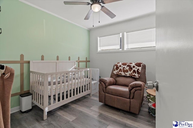 bedroom featuring ornamental molding, a crib, wood finished floors, and a ceiling fan