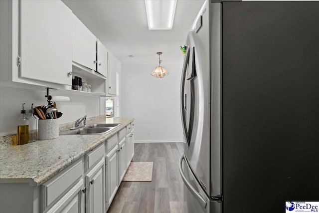 kitchen featuring baseboards, freestanding refrigerator, light wood-type flooring, white cabinetry, and a sink