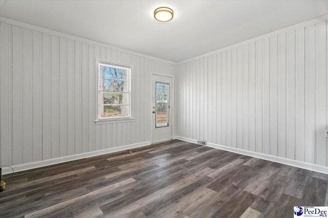 empty room with ornamental molding, dark wood-type flooring, visible vents, and baseboards