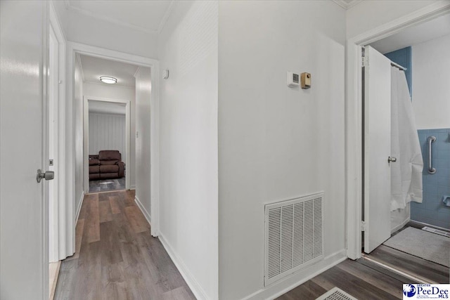 hallway featuring ornamental molding, visible vents, baseboards, and wood finished floors